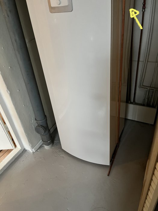 Rundat badkar delvis synligt bakom en dörröppning med synliga rör och betonggolv.