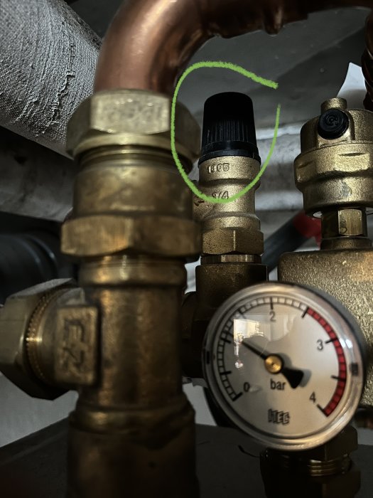 VVS-installation med kopparledningar, mässingsventiler och tryckmätare markerad med grön cirkel.