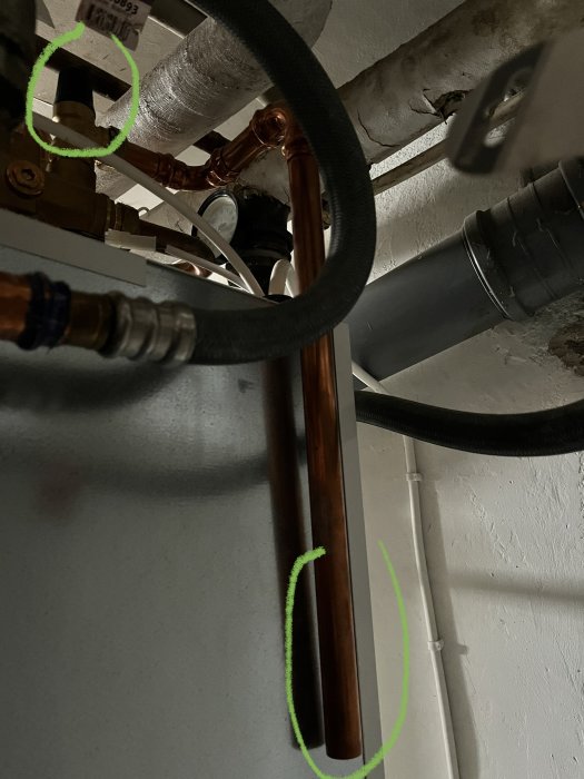 Rörinstallation med kopparledningar och isolerade rör, markerade med gröna cirklar för att visa specifika delar.