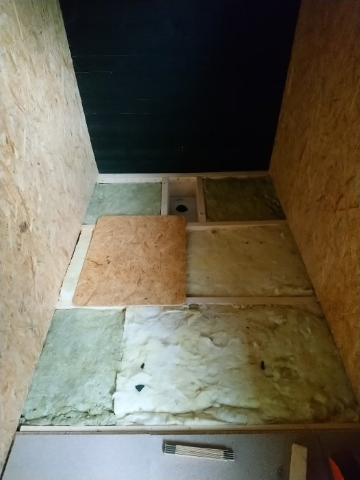 Ett pågående byggprojekt med isoleringsmaterial och OSB-skivor i ett ofärdigt rum.