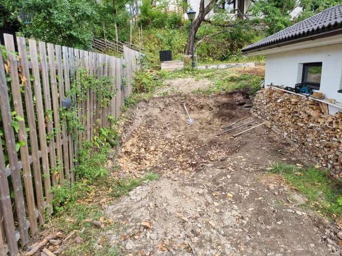 Uppgrävd trädgård etapp 1 inför vattenkassetter, med spade och hög vedstack.