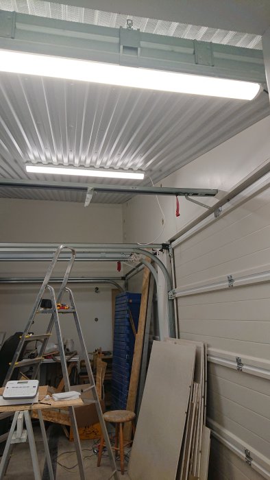 Inredning av ett garage med isolerade väggar och LED-belysning i taket, en stege och byggmaterial.