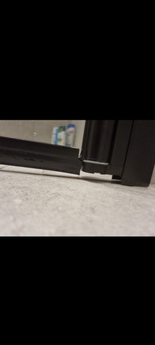 Ena sidan av en duschdörr är upphöjd från golvet, synlig avvikelse i passformen.