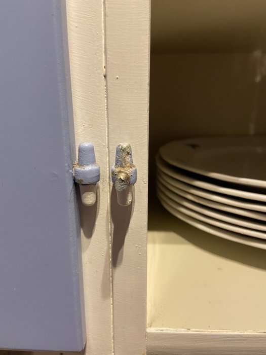 Avbruten skruv på en skåpluckas kant bredvid vita tallrikar.