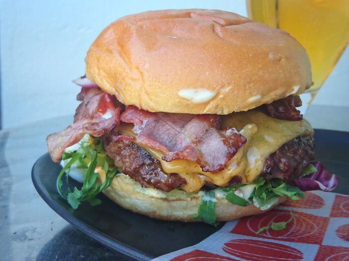 Juicy cheeseburger with bacon, cheese, greens on a bun, served on a plate with a drink in the background