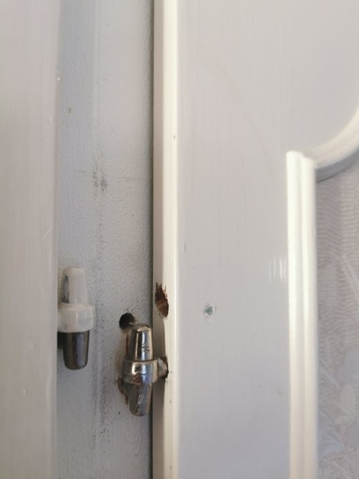 Vit garderobsdörr med metallgångjärn och slitage vid skruvfästet, köpta på jem&fix.