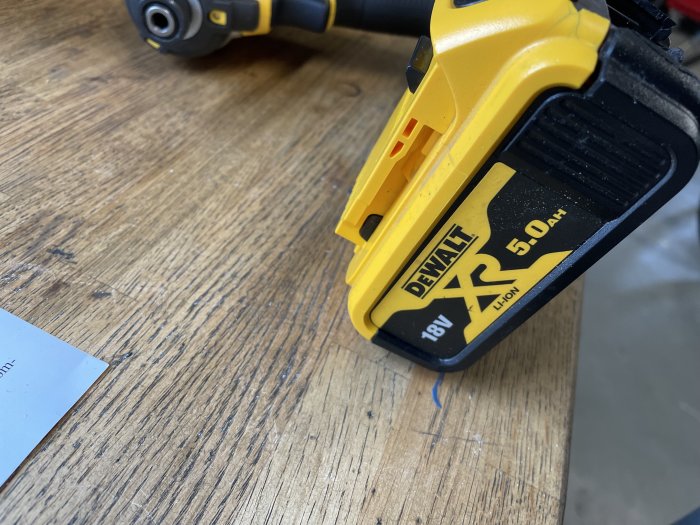 Gul och svart DeWalt 18V XR 5.0Ah Li-ion batteri monterat på en skruvdragare, på ett träbord.