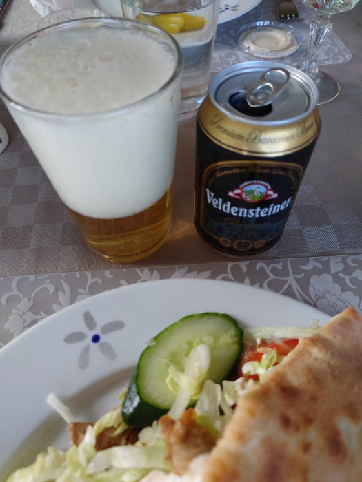 Ett glas bayersk pilsner med skum och en öppen burk Veldensteiner med maträtt i förgrunden.