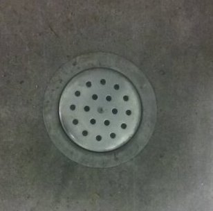 Rostfri avloppsbrunn i betonggolv med synlig brunnsil och uppjuten kant.