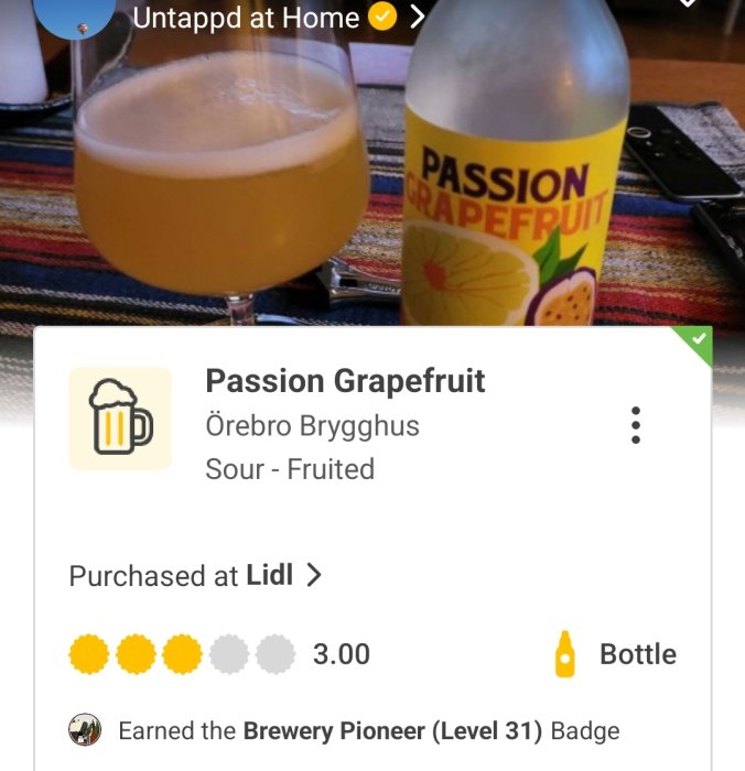 En öppen flaska och ett glas med suröl märkt "Passion Grapefruit" från Örebro Brygghus på ett bord.