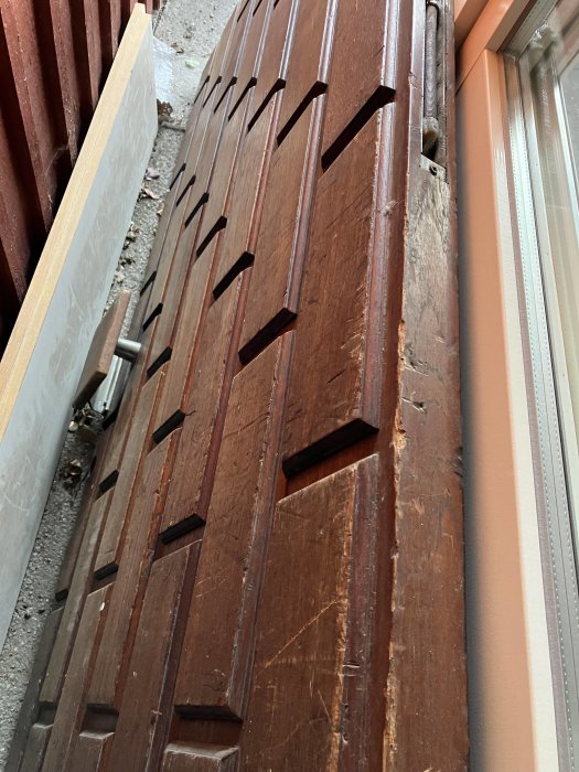 Staplad mörkbrun trädörr med utskurna detaljer, lutad mot en vägg nära ett fönster.