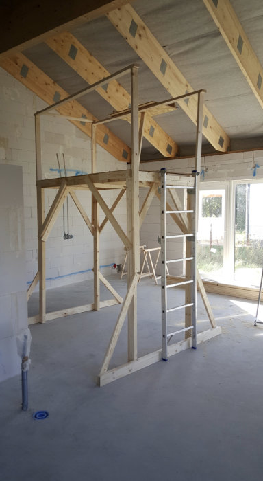 Arbetsplattform under konstruktion i ett rum under renovering, med träställning och en stege monterad på sidan.