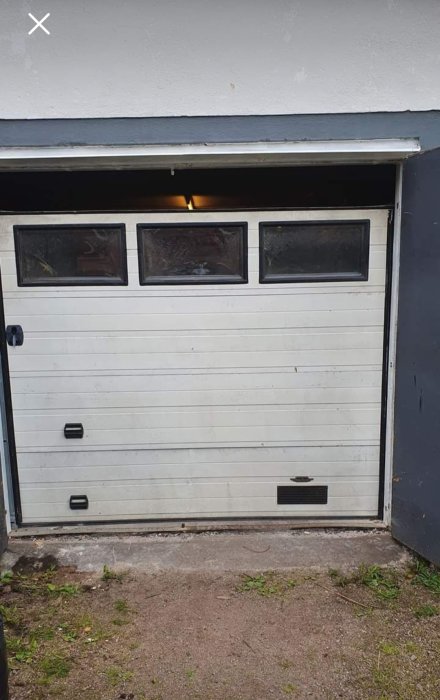 Garageport i vit metall med fönster och en mindre dörr integrerad i porten.