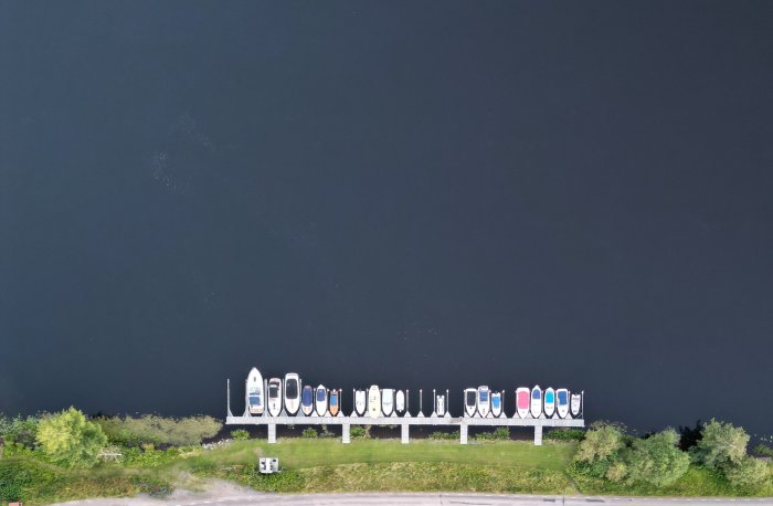 Flygbild av båtar uppradade på en brygga längs en mörk vattenyta.