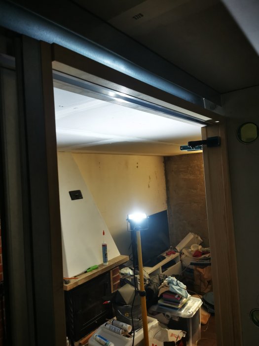 Garage under renovering med öppen dörr, rörligt arbetsljus och oorganiserade byggmaterial.