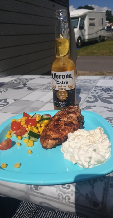 Grillad kyckling med sallad och tsatsiki på tallrik, Corona-öl med lime, bakgrund med husvagn.