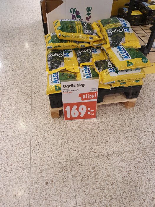 Pall med säckar av ogräsmedel märkta "Ogräs 5kg" och skylt med pris "169:-" i butik.