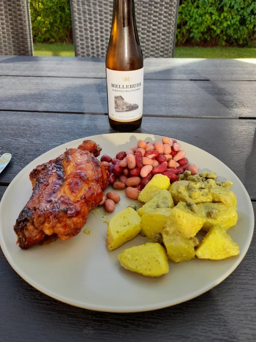 Grillade tjocka revben, pestoklädda potatisklyftor, bönmix och alkoholfri Mellerudspils på utomhusbord.