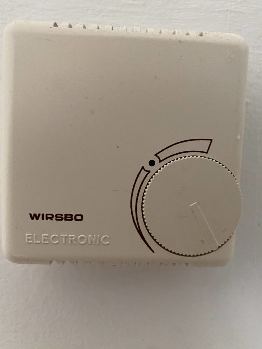 Väggmonterad Wirsbo termostat med ratten inställd nära en markerad ring.