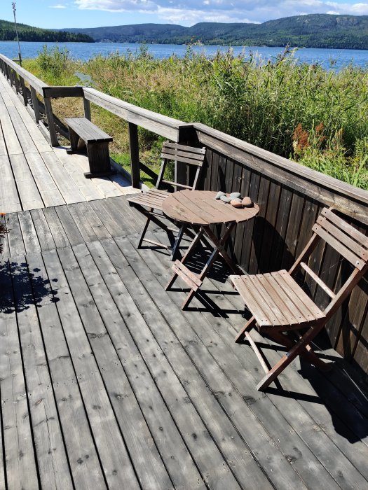 Slitet träcafeset på en terrass med utsikt över havet och grönska, i behov av ersättning.