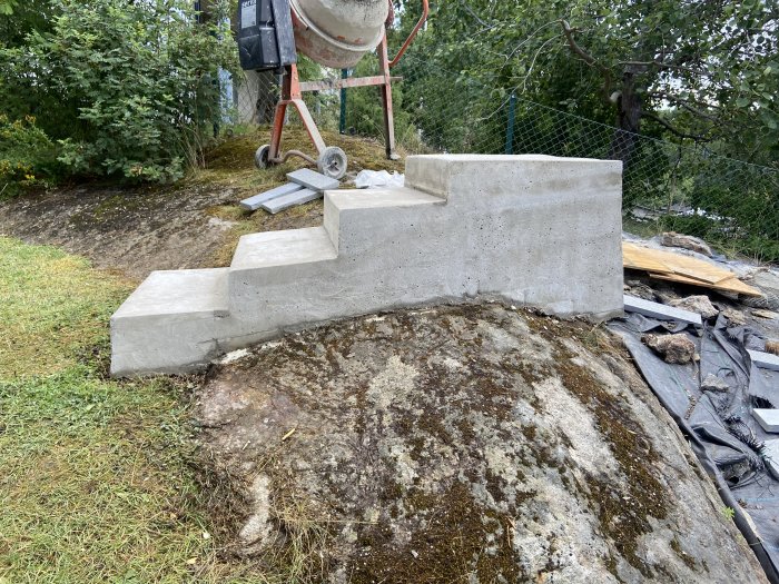 Nybyggd betongtrappa med fyra steg på en sluttande bergstomt, med byggmaterial i bakgrunden.