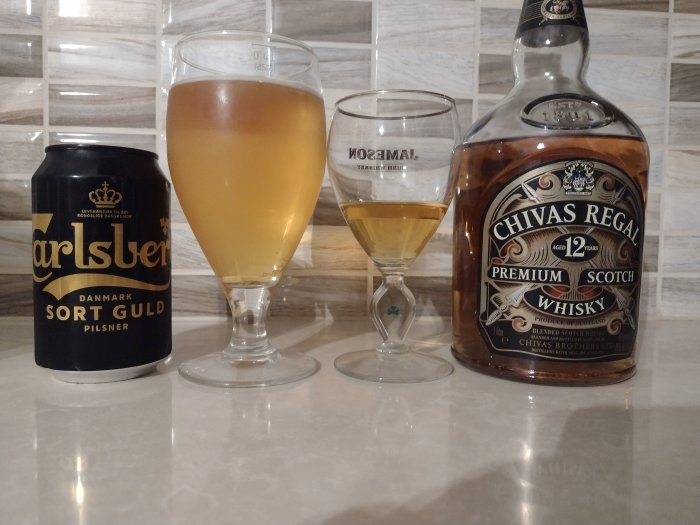 Burk Carlsberg Sort Guld öl, ölglas med hälften öl, whiskyglas med hälften whisky, Chivas Regal-flaska.