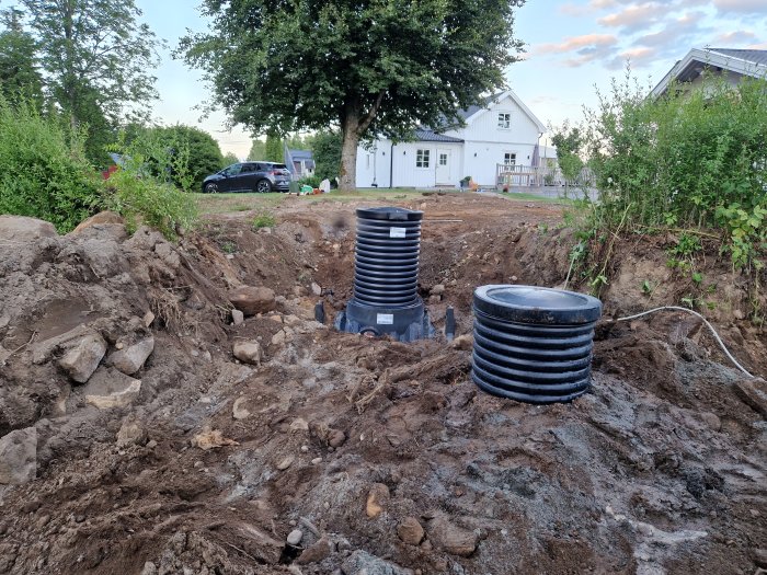 Installerad ny pipelife cistern i grävd schakt på en tomt, med gammal cistern bredvid och hus i bakgrunden.