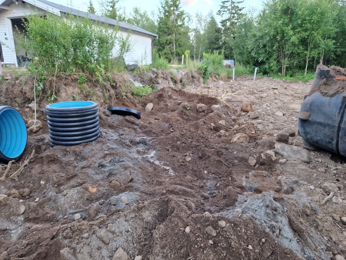 Nyinköpt svart Pipelife avloppstank på lerig byggplats med stenar och grävmaskin.