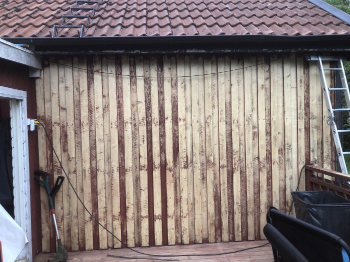 En fasad med vertikala plank där gammal plastfärg tagits bort, visar spåren efter fräsningen mot träytan.