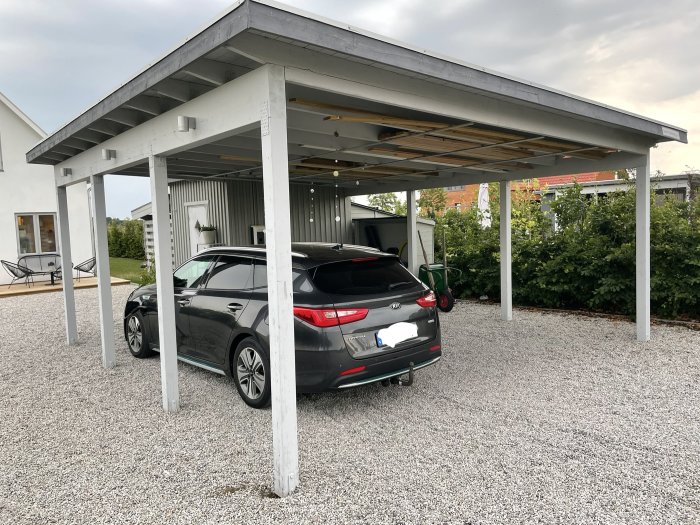 Bil parkerad under nybyggd fristående carport med vit stomme och grusad yta.