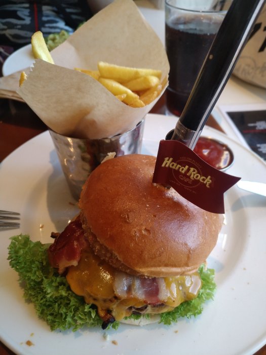 Hamburgare med ost och bacon på Hard Rock Café-tallrik med pommes frites och läsk.