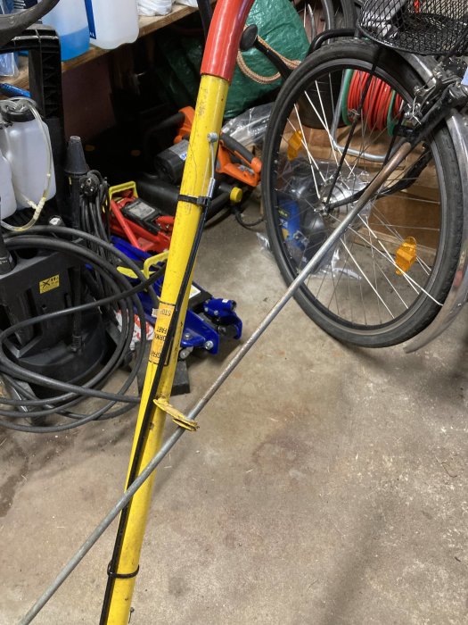 Gul cykelstång kopplad med vajer till cykels bromshandtag i en rörig garageverkstad.