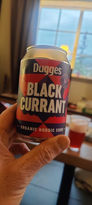 Hand håller en burk Dugges Black Currant Organic Nordic Sour med suddig bakgrund.