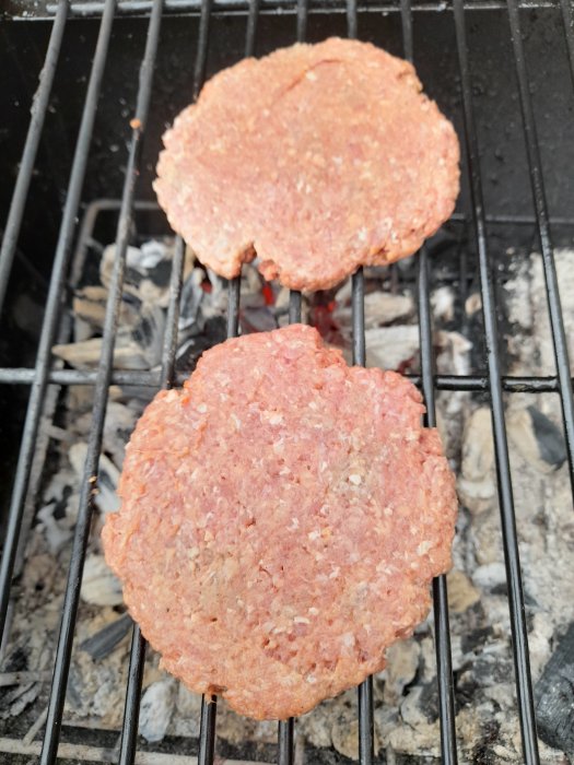 Två råa hamburgare på en kolgrill.