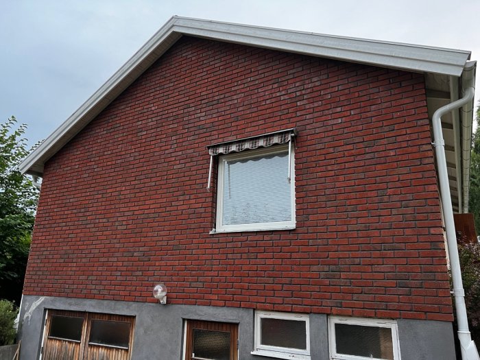 Husfasad med rött tegel och enstaka fönster, planerade borrlägen för ventilation och rörledningar är ej synliga.