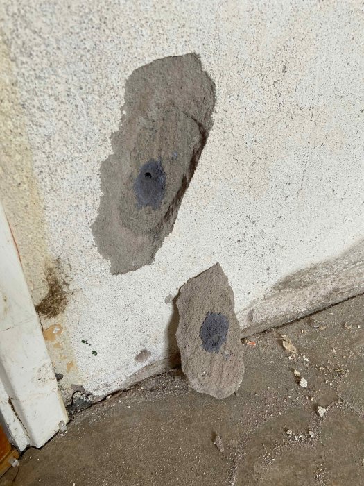Husgrund med lossnat putsstycke och avslöjat mörkare underlag.