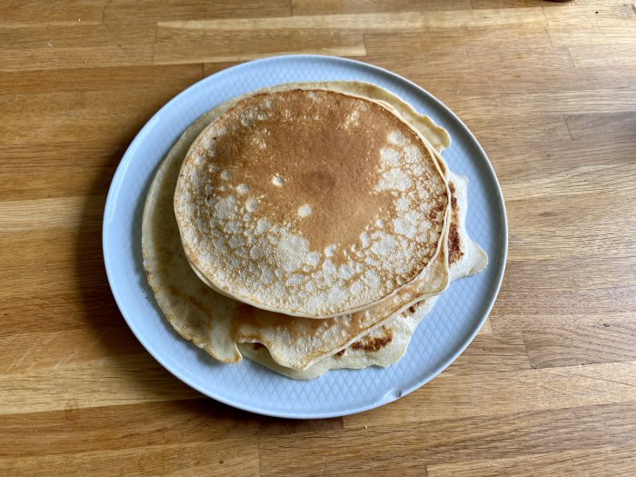 En tallrik med en hög amerikanska pannkakor på ett träbord.