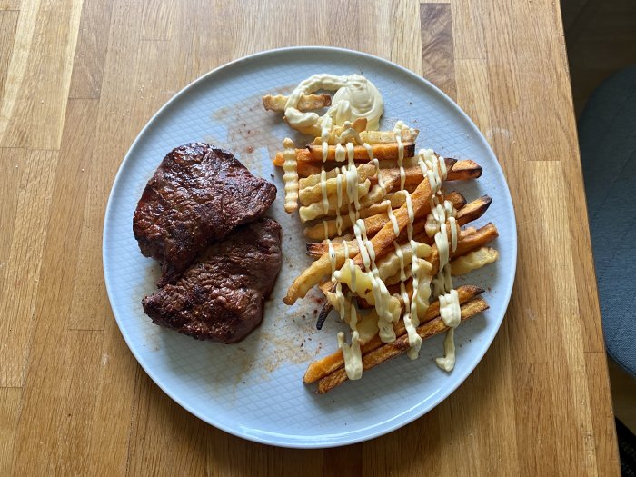 Grillad biff med pommes frites och majonnäs på en tallrik.