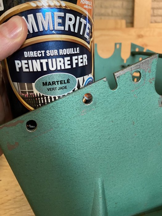 Hand håller en burk Hammerite-färg bredvid en maskindel med avflagande grön färg.