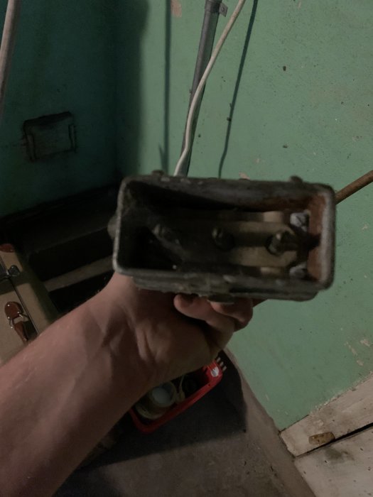 Hand håller en gammal och smutsig eluttagsdosa mot bakgrund av en grön vägg.