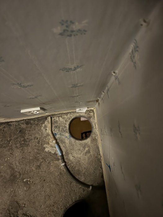 Håltagning i betong för avloppsrör nära golv och tak med synliga spårningsmärken och befintliga installationer.