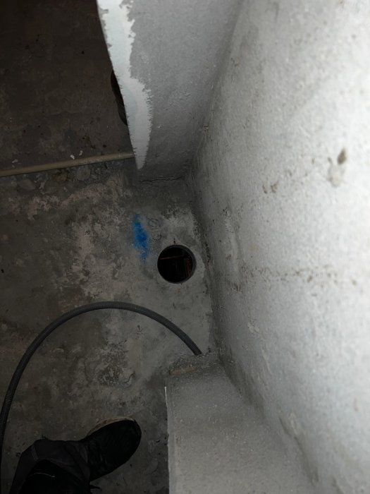 Överblick av nygjort hål i betongbjälklag för avlopp med synlig kabel och markeringar på golvet.