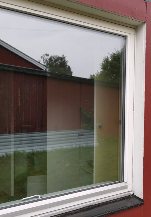 Utsikt genom ett dubbelfönster till en trädgård och reflektioner av omgivningen.