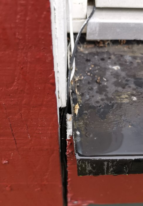 Närbild av fukt och skador runt ett fönster på en rödmålad vägg.