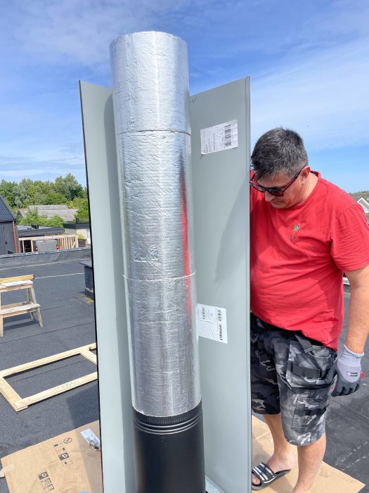 Man i röd tröja monterar isolerad ventilationskanal utomhus.