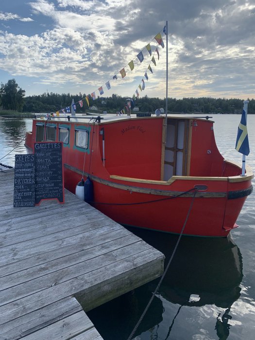 Röd matbåt med flaggor fastbunden vid brygga, meny visar "Galette", "Crepes" och drycker.