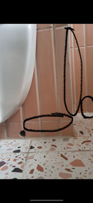 Urinal vid kakelvägg med terrazzomönstrat golv och sladd som leder till golvbrunn.