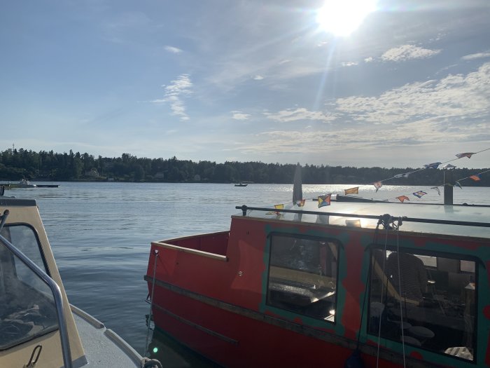 Röd matvagn vid en sjö med flaggdekorationer under en solig himmel, omgiven av båtar.