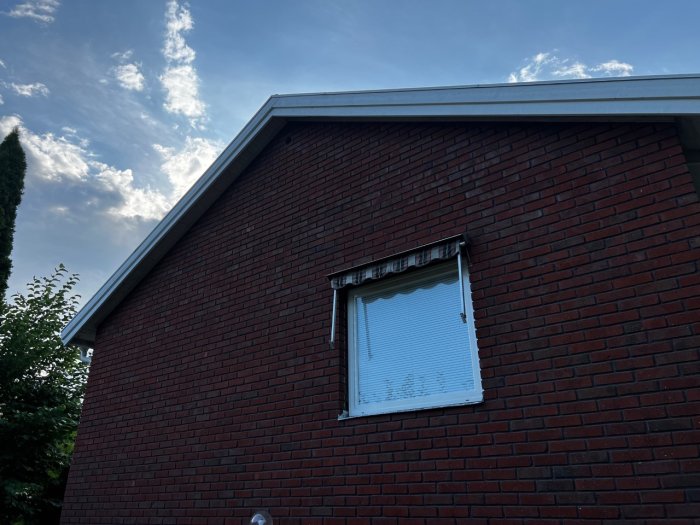 Husfasad med tegelvägg och ett fönster, visar plats för håltagning på vinden.