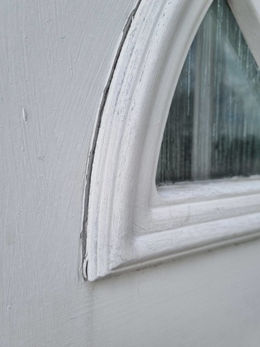 Närbild på ett fönsters träkarm med sprickor i färgen och slitage.